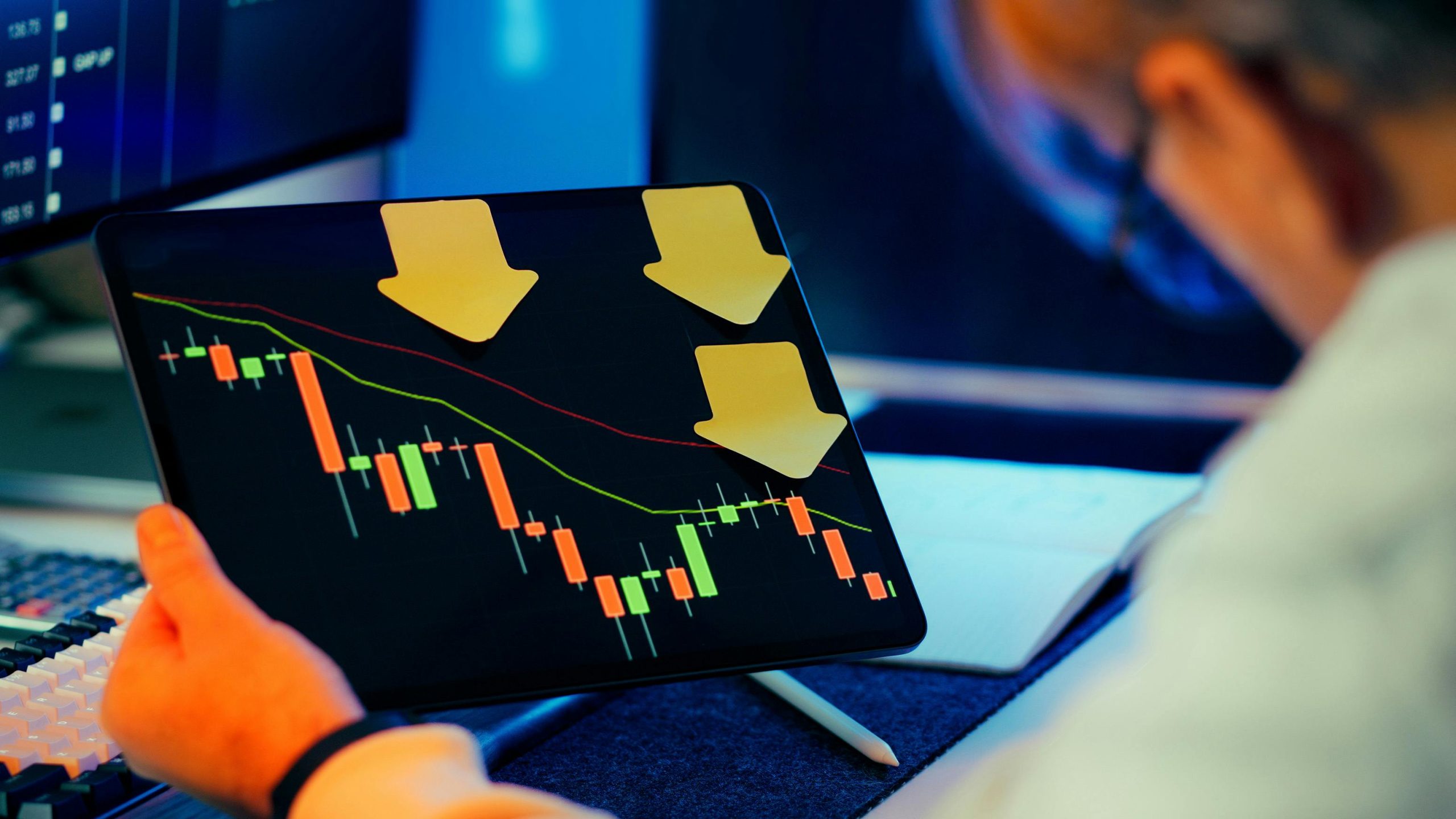 Tablet displaying a declining stock market chart with downward arrows during a market downturn.